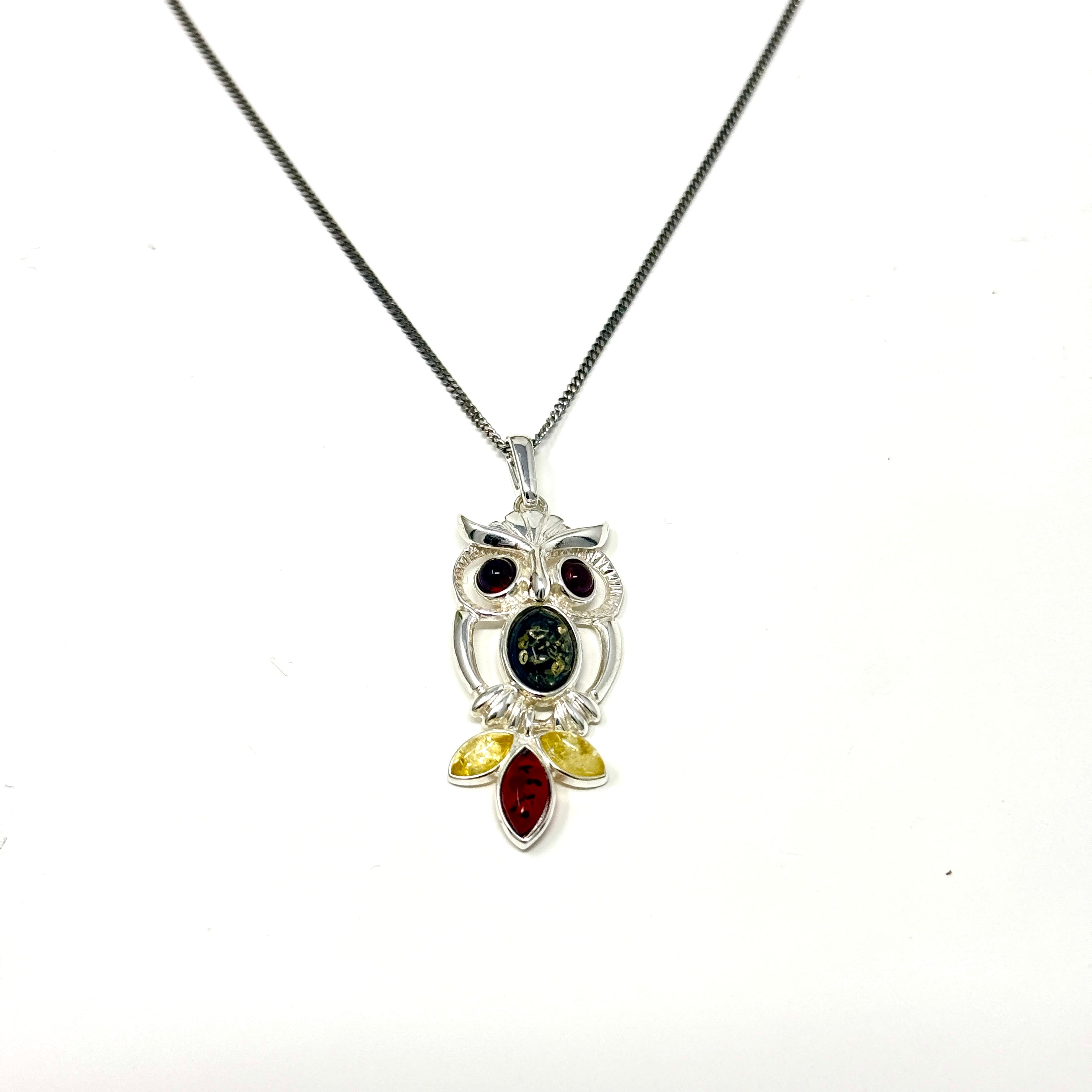 Silberne Halskette mit Eulen-Anhänger, verziert mit mehrfarbigem Bernstein in Braun, Gelb und Grün auf weißem Hintergrund.
