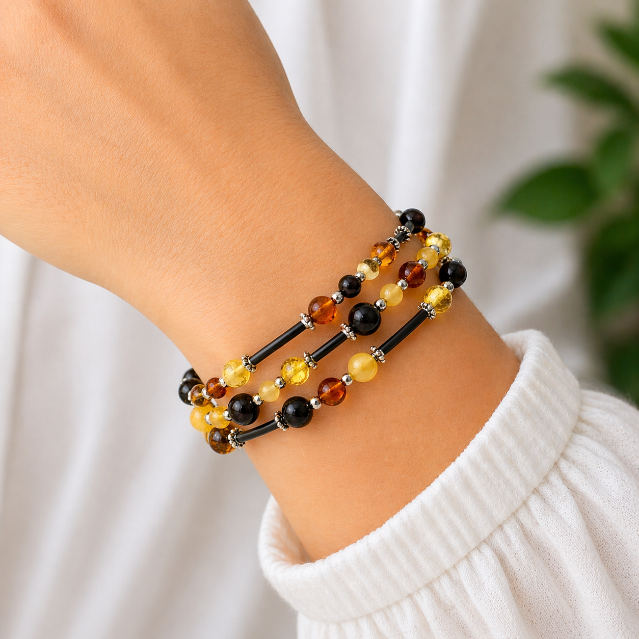 3-reihiges Bernstein Armband mit schwarzen Lederbändern und Bernsteinen in Gelb, Cognac und Schwarz am Handgelenk getragen mit silbernen Zwischenelementen