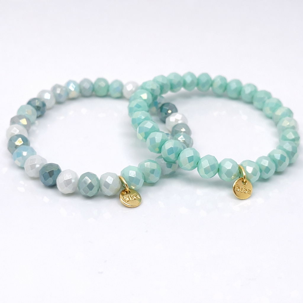 Zwei mintgrüne Biba Armbänder mit facettierten Perlen und goldenem Markenanhänger auf weißem Hintergrund