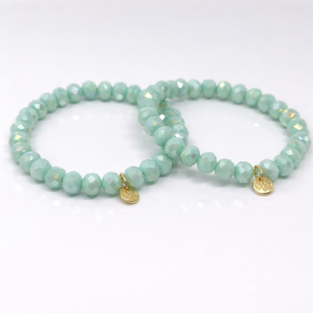 Mintgrünes Biba Armband mit facettierten Perlen und goldenem Anhänger auf weißem Hintergrund