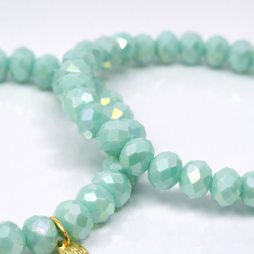 mintgrüne Biba Armbänder mit facettierten Perlen und goldenem Markenanhänger auf weißem Hintergrund
