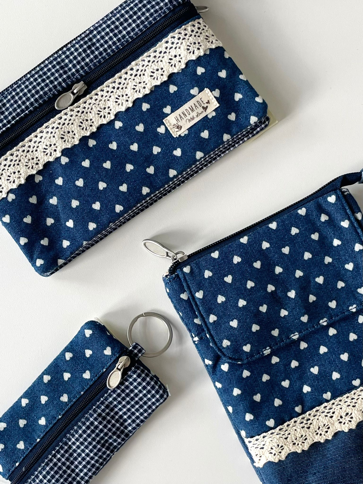 Handgemachtes Taschen-Set in Blau mit weißen Herzen, bestehend aus Schlüsselanhänger, Reißverschlusstasche und Umhängetasche mit Spitze.

